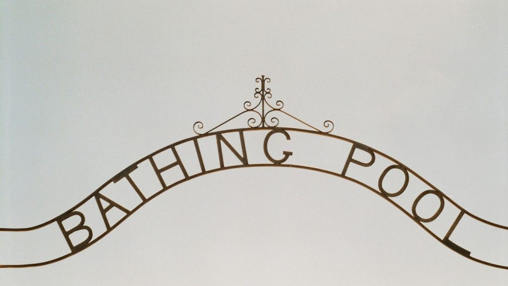 A sign that says bathing pool hanging from the side of a building