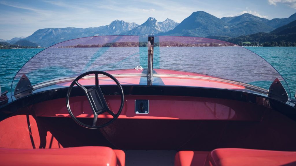 a red boat with a steering wheel on a body of water